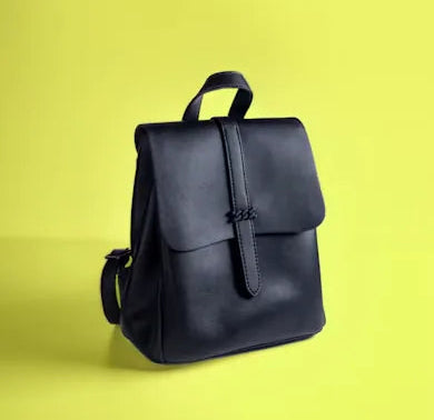 Small black flap-top backpack with a strap closure and top handle against a yellow-green background