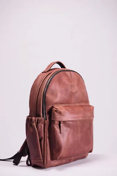 Brown leather backpack, side view, with an embossed logo, front zip pocket and side bottle pocket