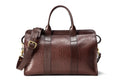 Brown pebbled leather duffel bag with leather handles, brass buckle and shoulder strap, front view