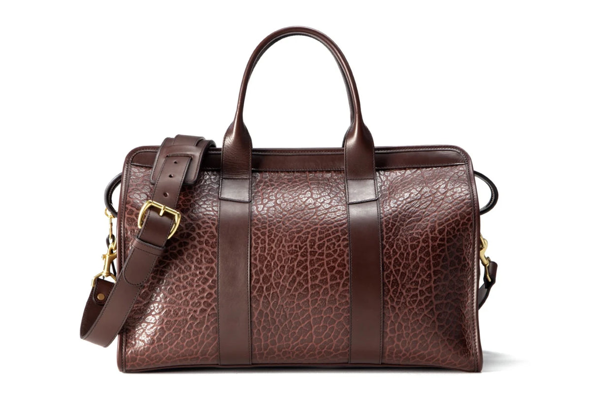 Brown pebbled leather duffel bag with leather handles, brass buckle and shoulder strap, front view