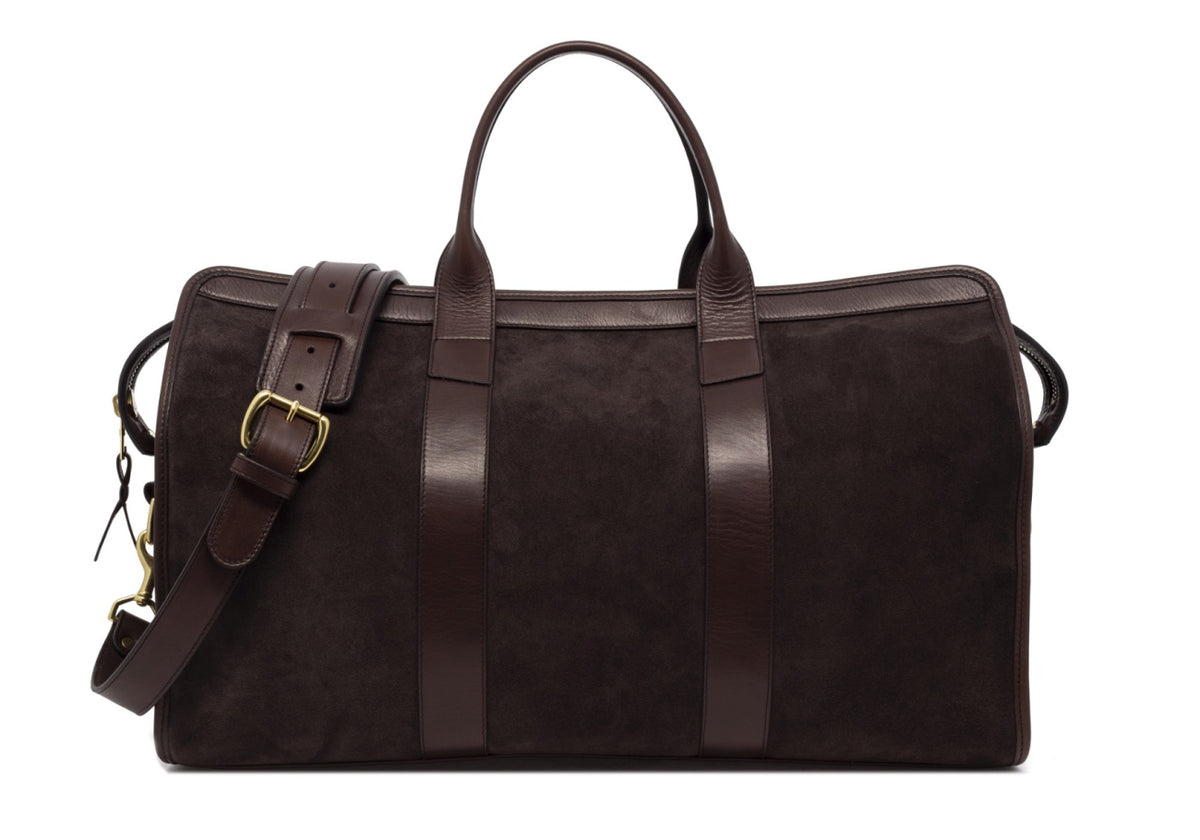 Dark brown suede duffel bag with leather handles, brass buckle and shoulder strap, front view